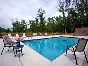 A rectangular swimming pool with a wooden fence, lounge chairs, and a table with a vase of flowers. - Modern Cabin in Pigeon Forge for a Romantic Glamping Rendezvous (Sevierville)