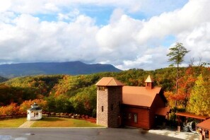 A lodge with a stone tower, a red-roofed main building, and a gazebo in a forested area with mountains in the background. - Modern Cabin in Pigeon Forge for a Romantic Glamping Rendezvous (Sevierville)