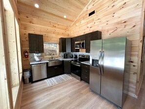 A compact kitchen with wooden walls, stainless steel appliances, and a small rug. - Modern Cabin in Pigeon Forge for a Romantic Glamping Rendezvous (Sevierville)