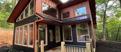 Une maison à deux étages avec un porche à l’avant, de grandes fenêtres et une terrasse en bois.