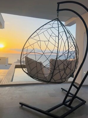 Ein kugelförmiger Hängekorb mit geometrischer Drahtstruktur, platziert auf einem Balkon mit Blick auf das Meer und einen Sonnenuntergang.