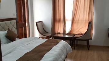 Un dormitorio con cama, dos sillas, una puerta de madera y una ventana con cortinas.