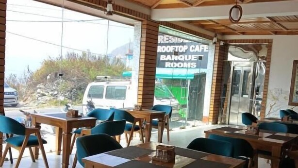 A restaurant with wooden tables and chairs, a visible menu board, and a view of the outside. - HOTEL KAMAL RESIDENCY BY UK SEASON (Tehri)