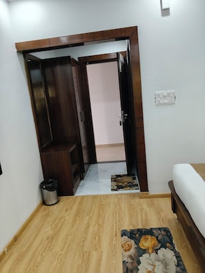 Quarto com guarda-roupa de madeira, cama, lixeira e porta para outro cômodo.