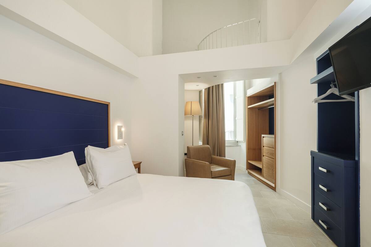 Une chambre d’hôtel avec un grand lit, une chaise, une armoire et un téléviseur.