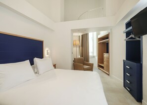 Quarto de hotel com uma cama grande, uma cadeira, um guarda-roupa e uma televisão.