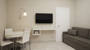 Un espace de vie compact comprenant une table à manger, des chaises, un canapé, un téléviseur fixé au mur et une porte.