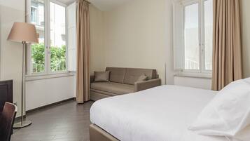 Una habitación de hotel con cama, sofá, lámpara y ventanas grandes.