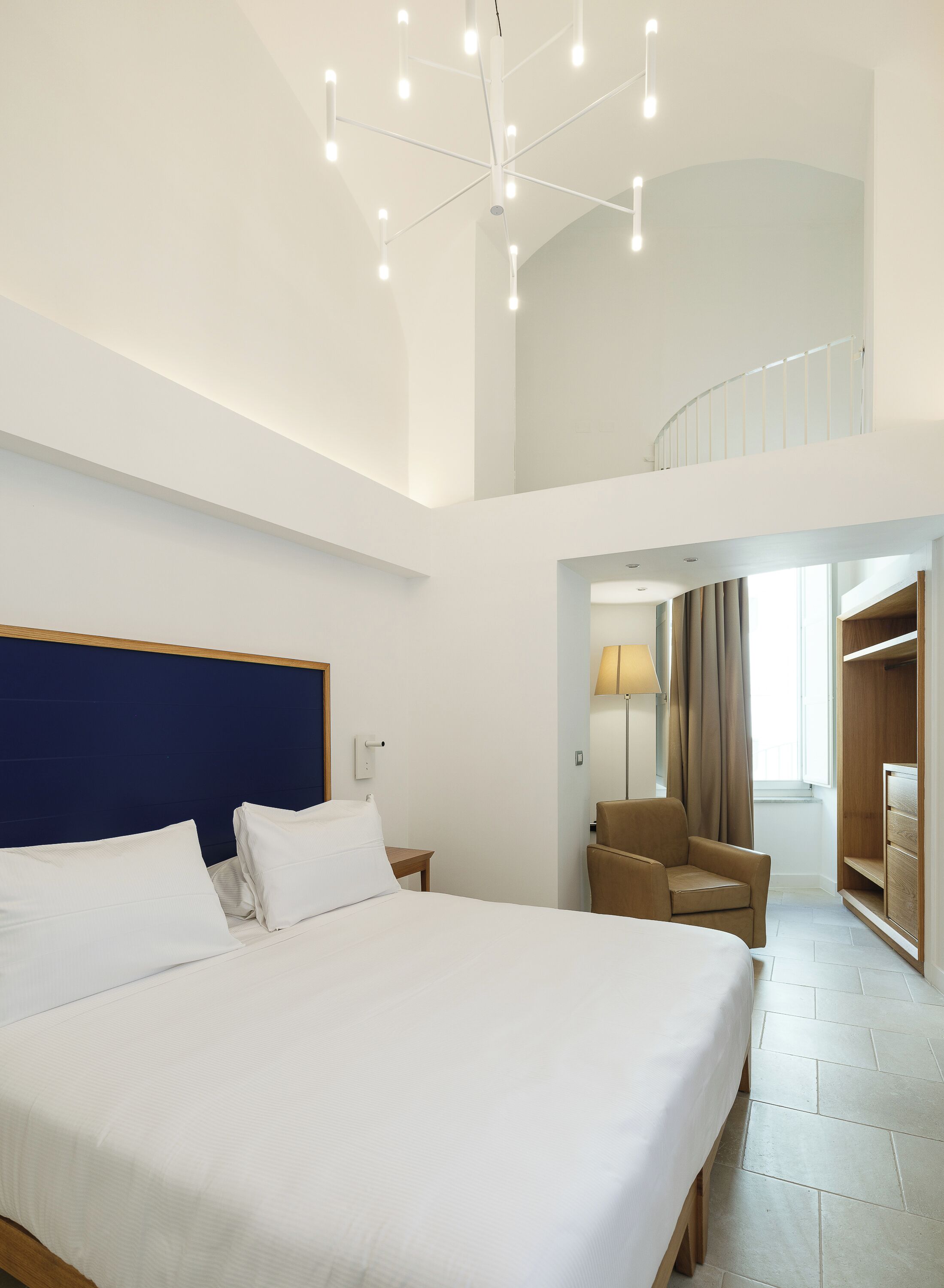 Una camera d'albergo moderna con un letto grande, una scrivania, una sedia, una lampada e vista sull'esterno.