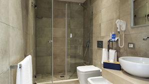 Une salle de bain moderne dotée d’une douche à parois de verre, de toilettes, d’un lavabo avec un grand bac et d’un sèche-cheveux fixé au mur.