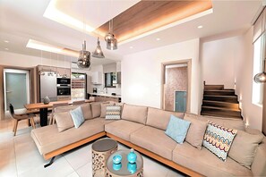 A modern living room with a sectional sofa, a glass coffee table, and pendant lighting. - Minoas Sea Villa Heated Pool (Lake Kournas)