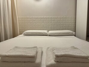 A neatly made bed with white linens and pillows, a white textured headboard, and two folded towels on the bed. - Rome Center Near Termini and the Colosseum: Private Room & Bath, Best Price (Roma)