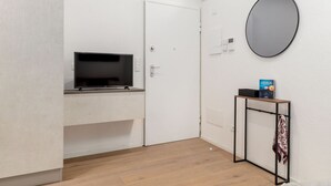 A room with a TV on a stand, a door, a mirror, and a small table with a book. - A comfortable and welcoming 30 square meters studio apartment, perfect for three people, located on the fourth floor of a renovated building (no elevator).The property is situated in the heart of Modena (within the ZTL restricted traffic zone); it is an  (Modena)