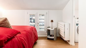 A bedroom with a red bed, a small table with a lamp, a radiator, and a washing machine. - A comfortable and welcoming 30 square meters studio apartment, perfect for three people, located on the fourth floor of a renovated building (no elevator).The property is situated in the heart of Modena (within the ZTL restricted traffic zone); it is an  (Modena)