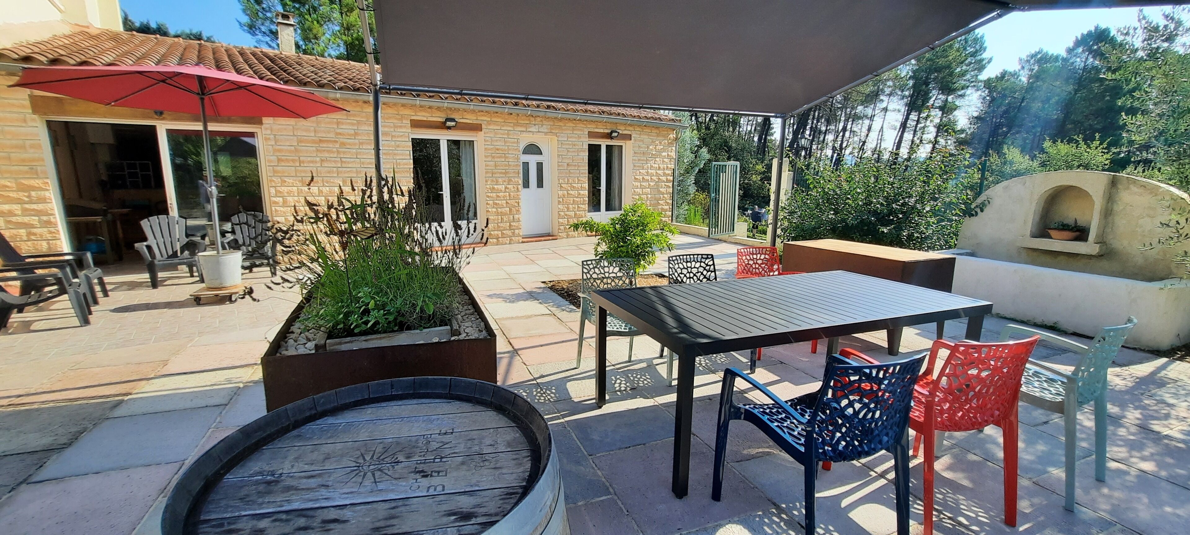 An outdoor patio with a table and chairs, a red umbrella, and a stone building in the background.