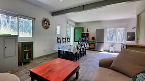 Zona d'estar àmplia amb taula de dinar, cadires, sofà, televisió i cuina amb armaris i nevera.
