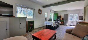 Ein geräumiger Wohnbereich mit Esstisch, Stühlen, einer Couch, einem Fernseher und einer Küchenzeile mit Schränken und einem Kühlschrank.