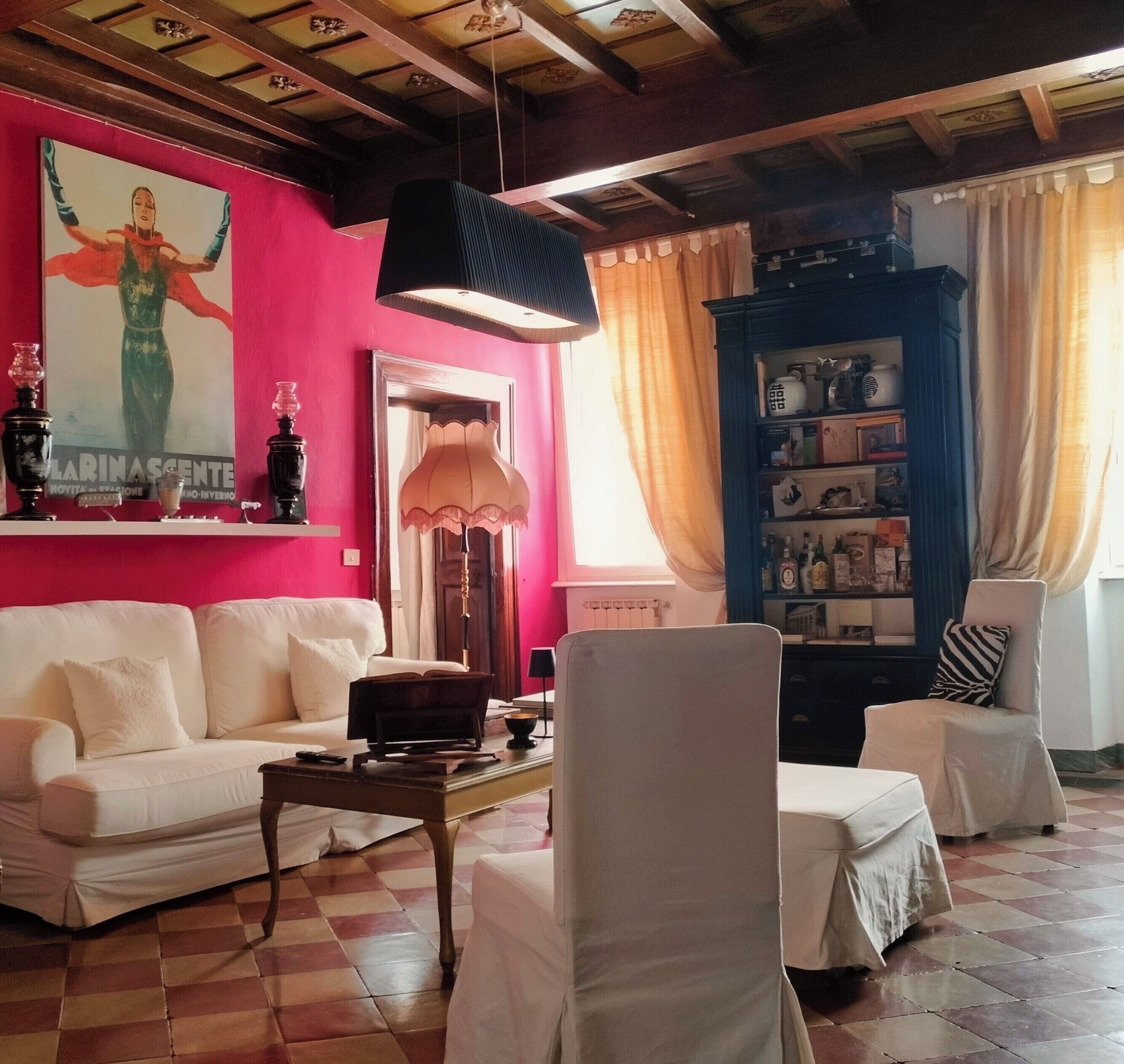 A living room with a white sofa, a coffee table, a bookshelf, and a large painting on the wall.