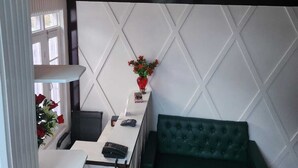 Un área de recepción con un mostrador, un sofá verde, un techo decorativo y una pared con diseño geométrico.