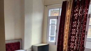 Una habitación de hotel con cama, cortinas en la ventana, mesita de noche y cabecera.