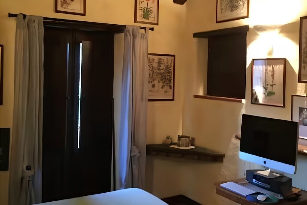 Una camera d'albergo con un letto, una scrivania con un computer, una finestra con tende e opere d'arte appese al muro.