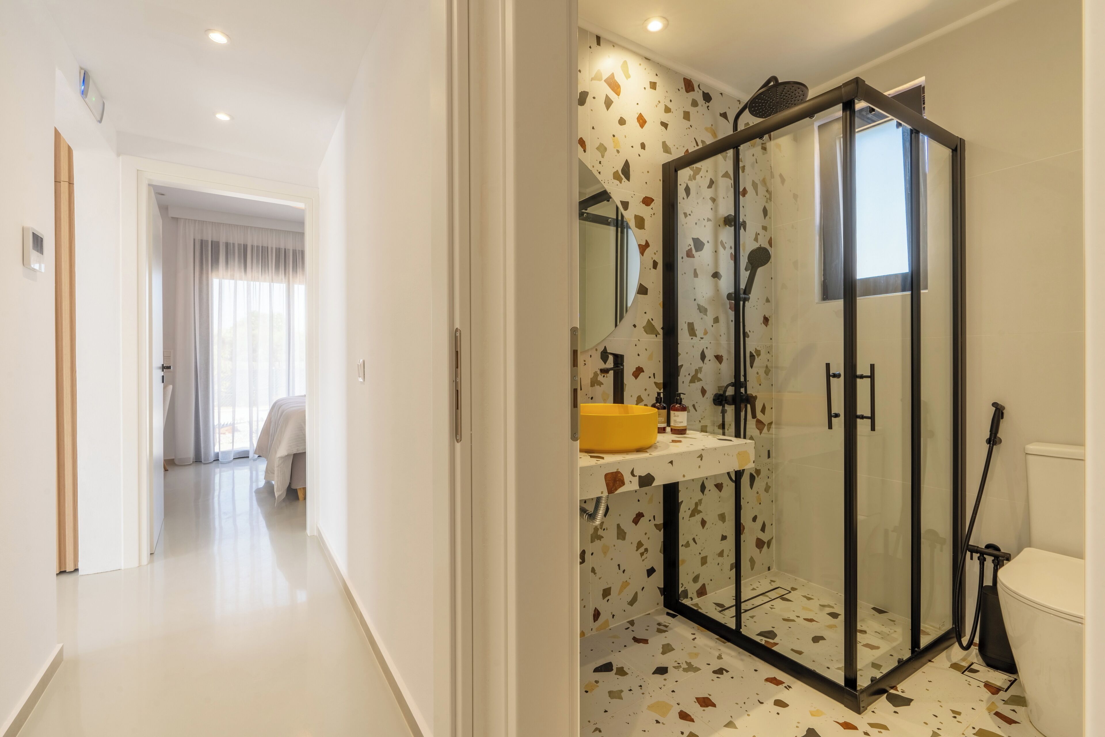 Un baño moderno con cabina de ducha de vidrio, lavamanos amarillo y un inodoro.