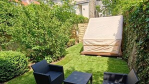 A backyard with a small patio area, a covered sleeping area, and surrounding greenery.