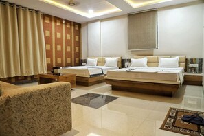 Quarto de hotel com duas camas, um sofá, uma mesa de centro e um tapete decorativo.