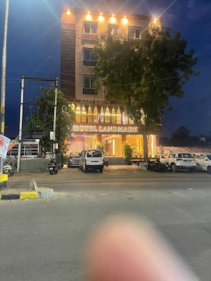 A multi-story building with a sign reading 'HOTEL LANDMARK.' There are parked cars and a tree in front.