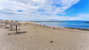 A beach with lounge chairs and umbrellas, a rocky breakwater, and a clear sky. - Pueblo Canario Ocean Breeze Apartment (Playa de las Américas)