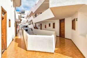 A narrow corridor with white walls and a tiled floor, leading to a building with balconies. - Fabulous brand new apartment in Parque Royal (Costa Adeje)
