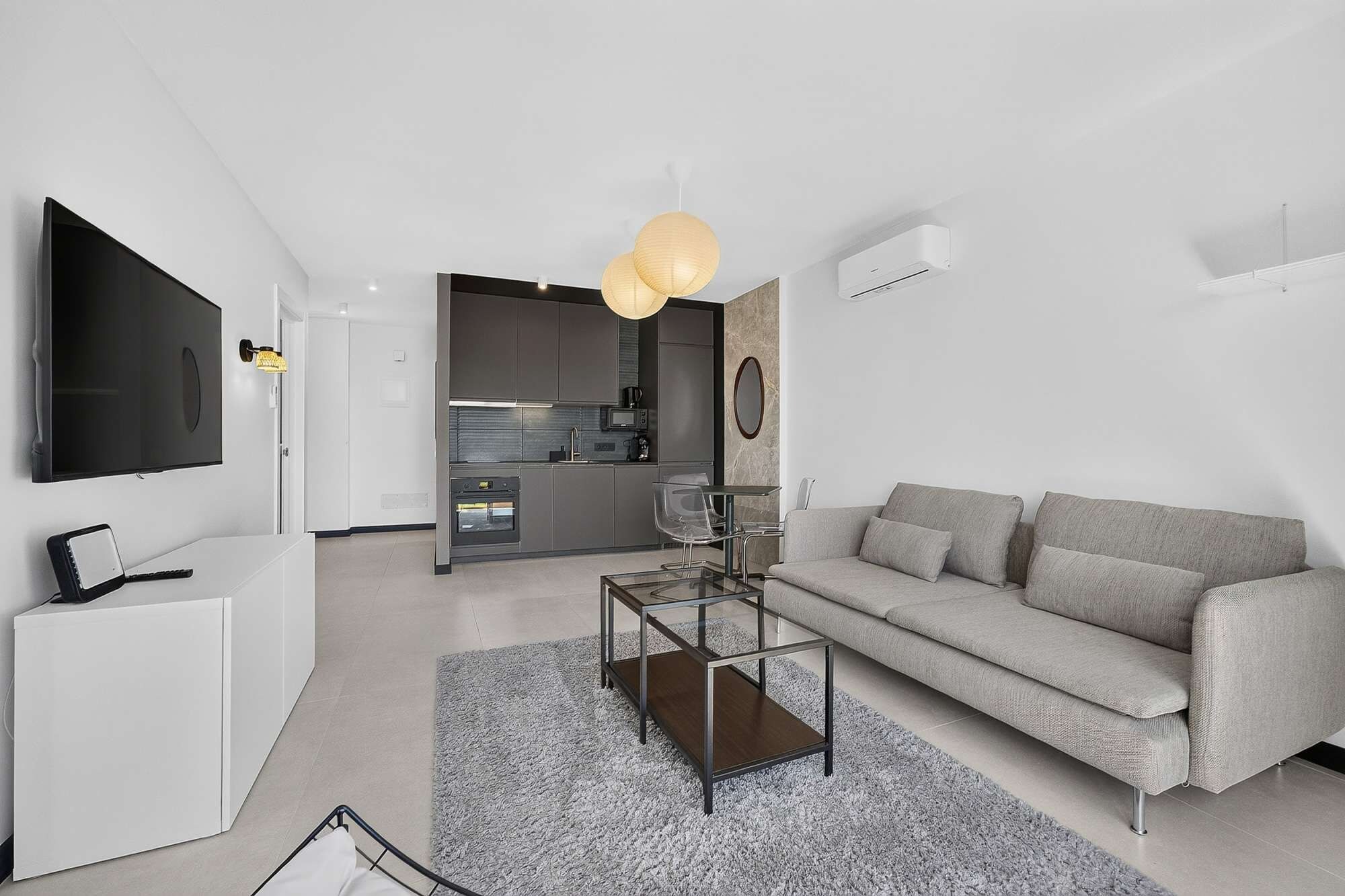 Un salon moderne avec un canapé gris, une table basse en verre et un téléviseur à écran plat fixé au mur.