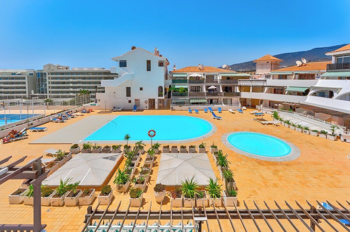 Ein Resort mit einem großen Schwimmbad, Liegestühlen und einem weißen Gebäude mit Balkonen.