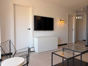 Ein modernes Wohnzimmer mit einem weißen Sofa, einem Glastisch, einem schwarzen, an der Wand befestigten Fernseher und einem weißen Schrank.