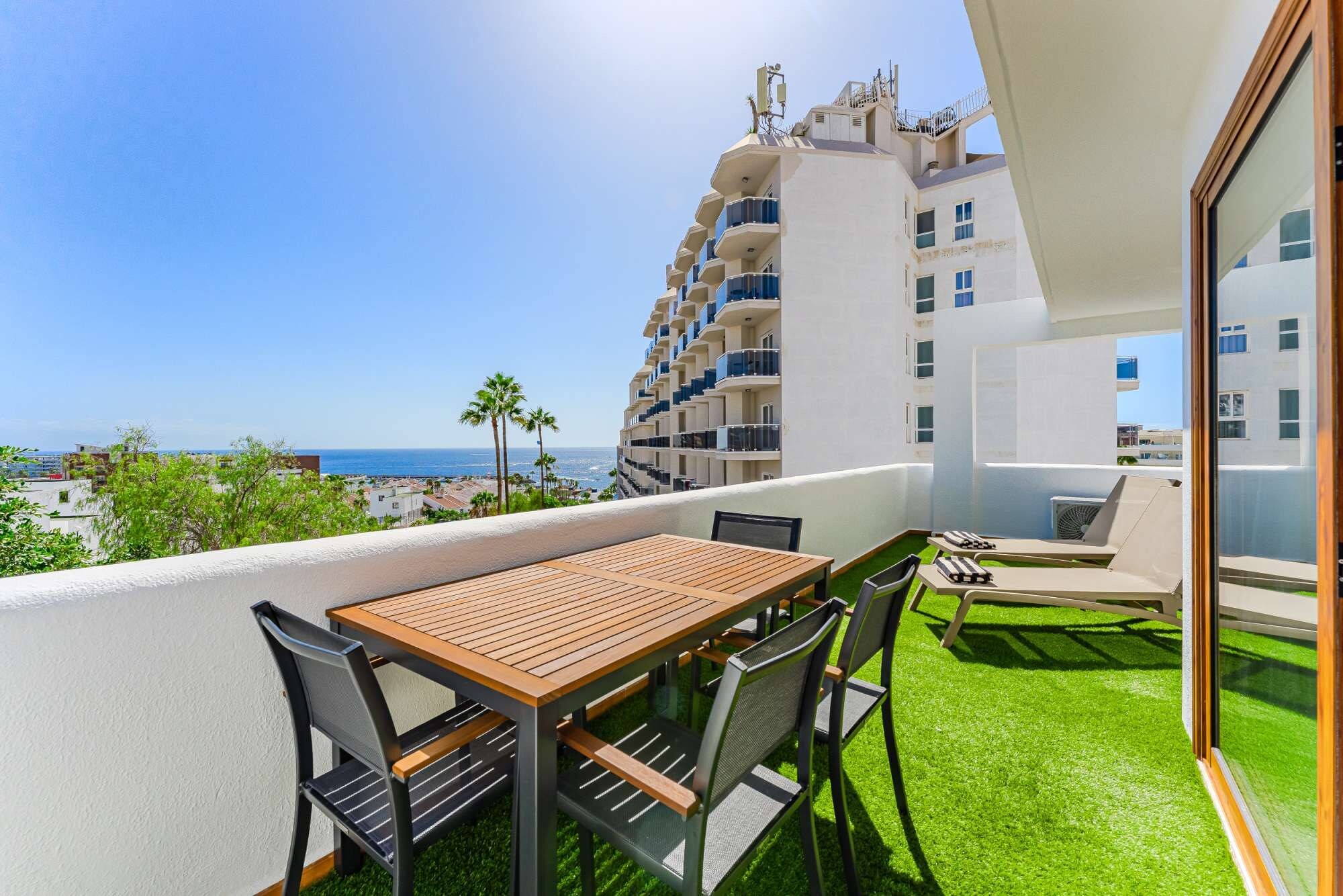 A balcony with a wooden table and chairs, overlooking a coastal cityscape.