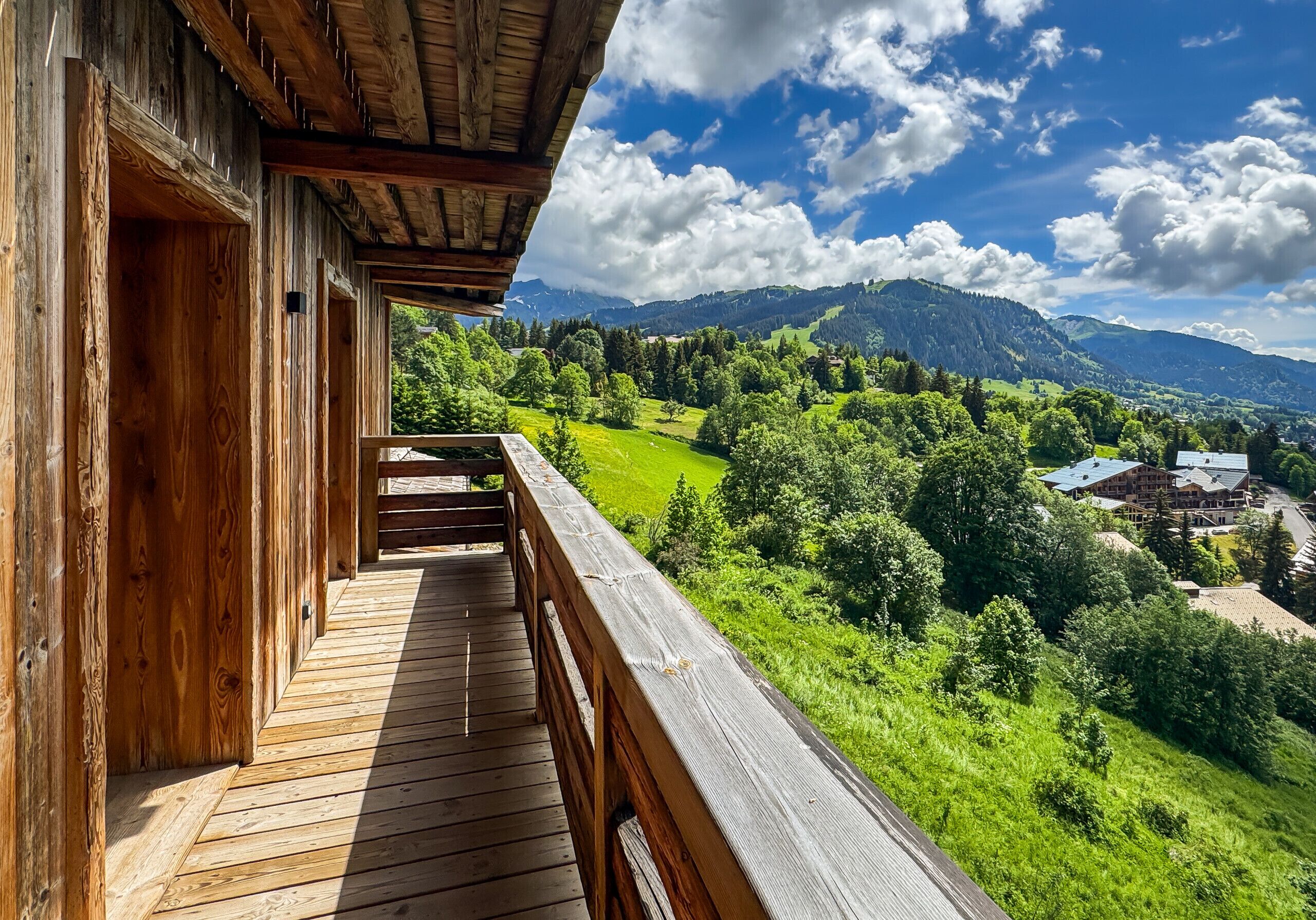 Un balcon en bois offrant une vue sur une vallée verdoyante et des montagnes.