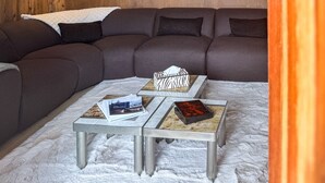 A modern living room with a sectional sofa, two side tables, a chandelier, and a white furry rug. - Coeur de Mage: Stunning View of Megève (Megève)