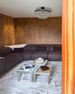 A modern living room with a sectional sofa, two side tables, a chandelier, and a white furry rug. - Coeur de Mage: Stunning View of Megève (Megève)