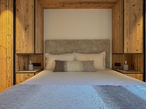 A bedroom with a wooden headboard, a bed with two pillows, and nightstands with lamps. - Nid du Mage: Breathtaking View of Megève (Megève)