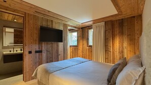 A wooden room with a bed, a TV mounted on the wall, and a window with curtains. - Coeur de Mage: Stunning View of Megève (Megève)