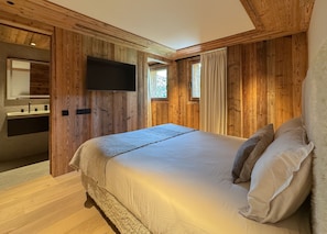 A wooden room with a bed, a TV mounted on the wall, and a window with curtains. - Coeur de Mage: Stunning View of Megève (Megève)