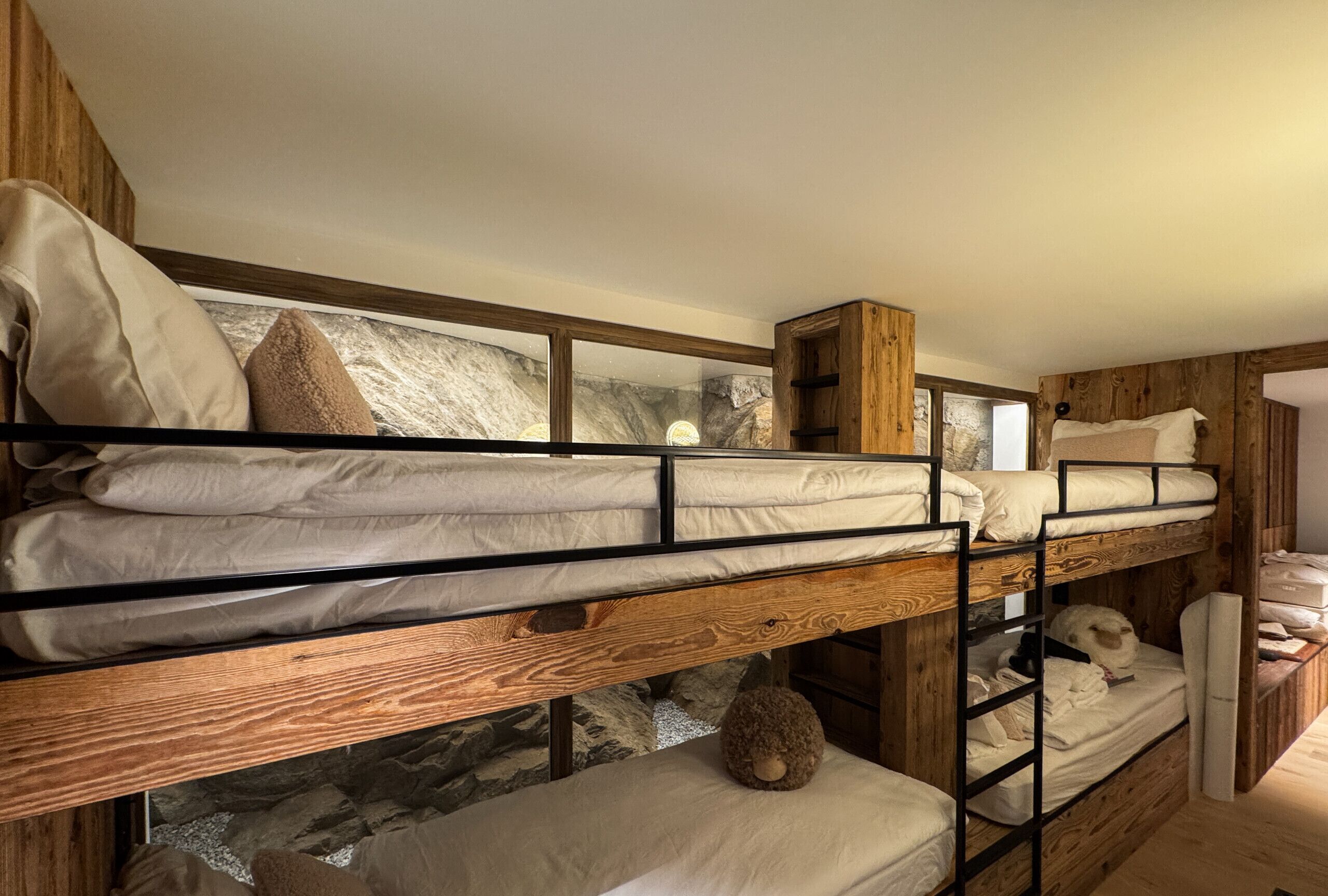 A bunk bed room with wooden walls, a stone wall, and a window.