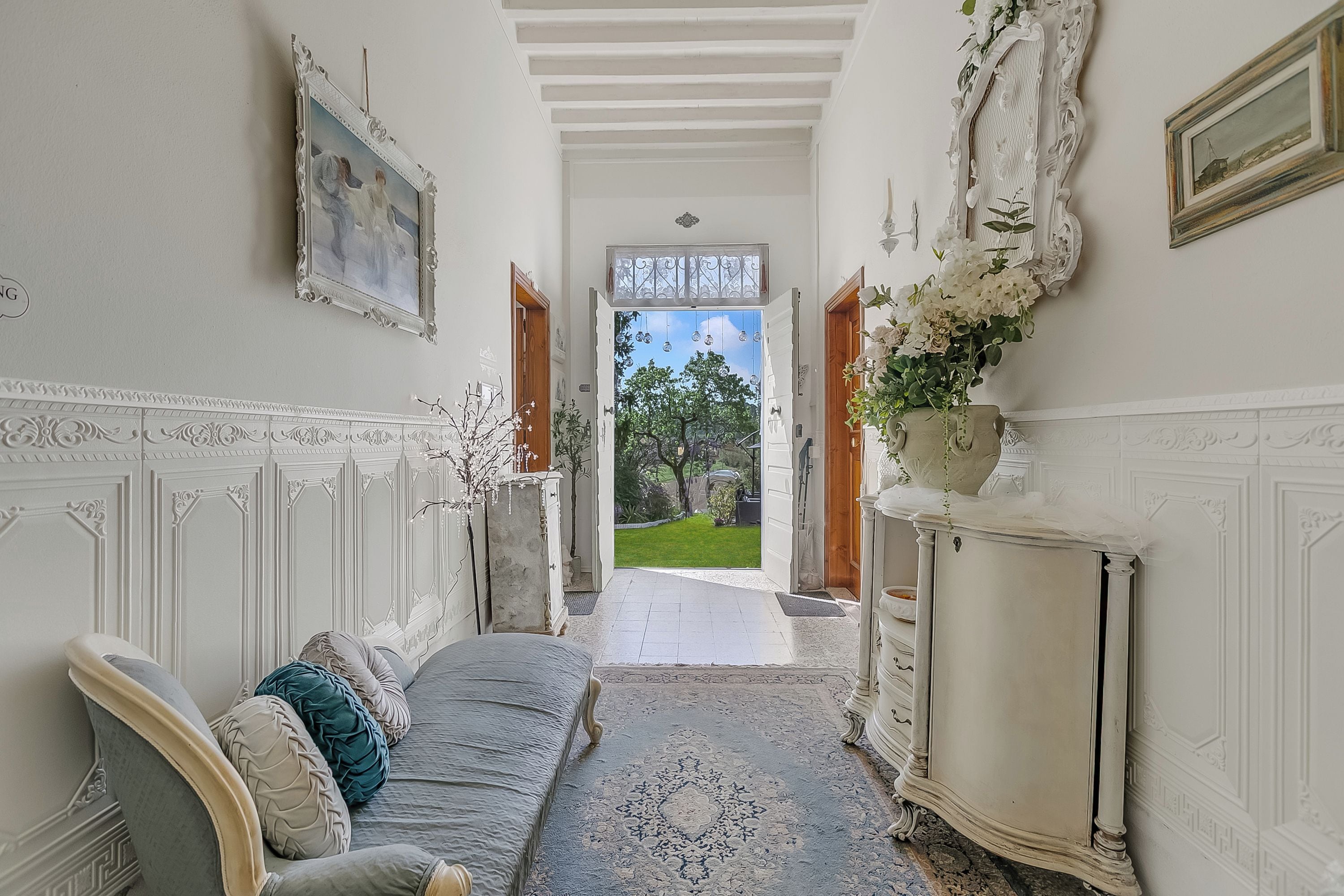 A hallway with a bed, a dresser, a mirror, and a door leading to a garden.