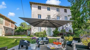 En udendørs terrasse med siddepladser, et bord med drikkevarer og en stor parasol.