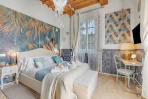 Ein Schlafzimmer mit einem großen Bett, einem Schreibtisch, einem Stuhl, einer Chandelier und Blick ins Freie.
