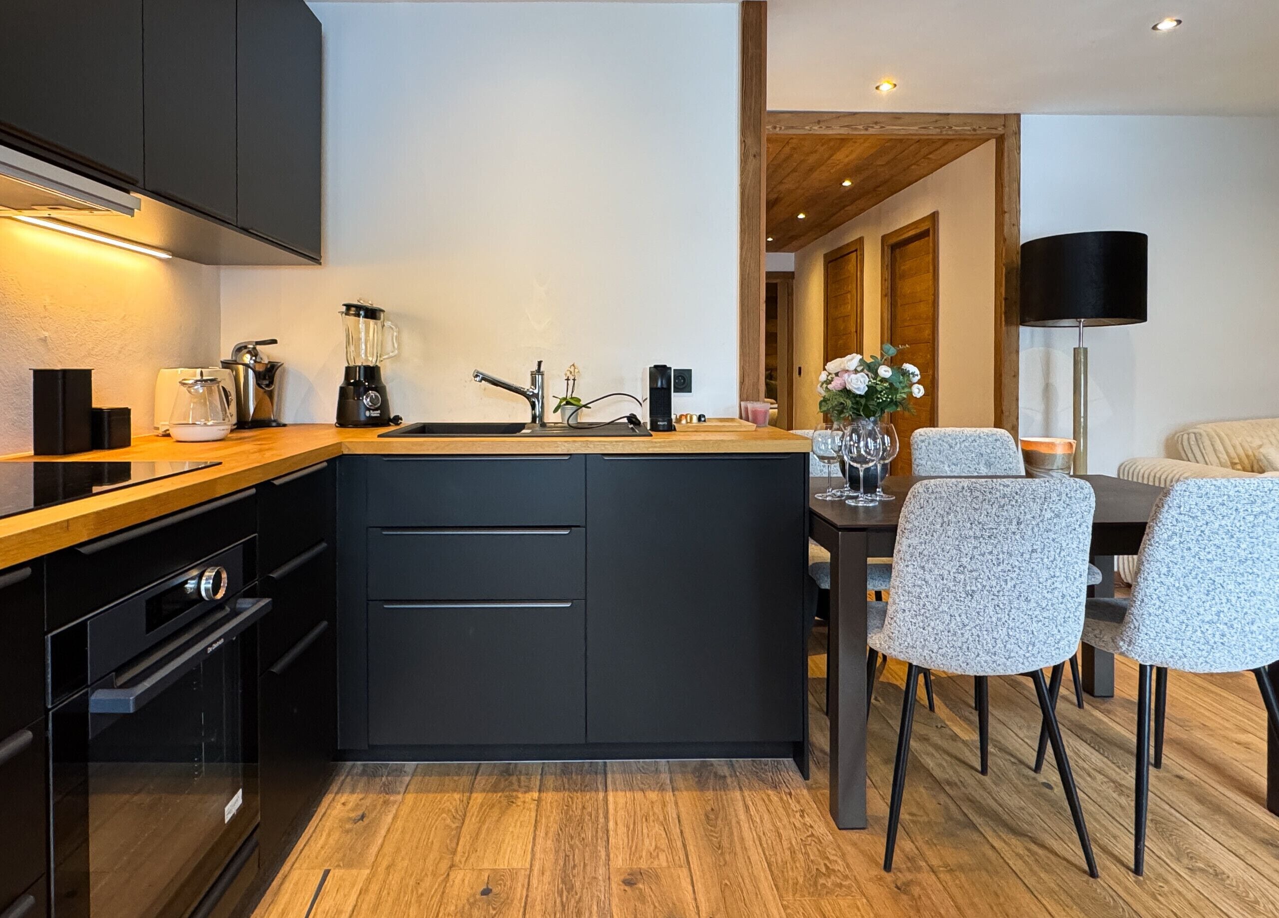 A modern kitchen with a central island, black cabinetry, and a dining area with a table and chairs.
