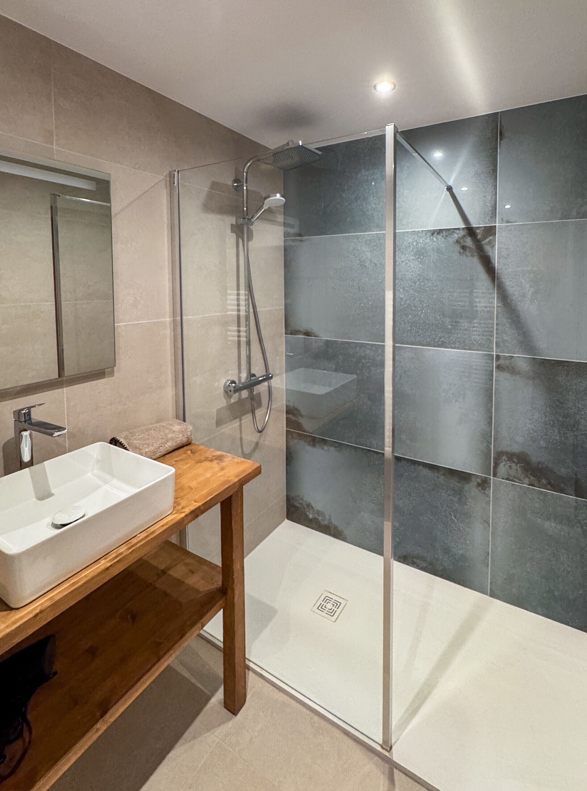 A modern bathroom with a glass shower enclosure, a wooden vanity, and a large mirror.