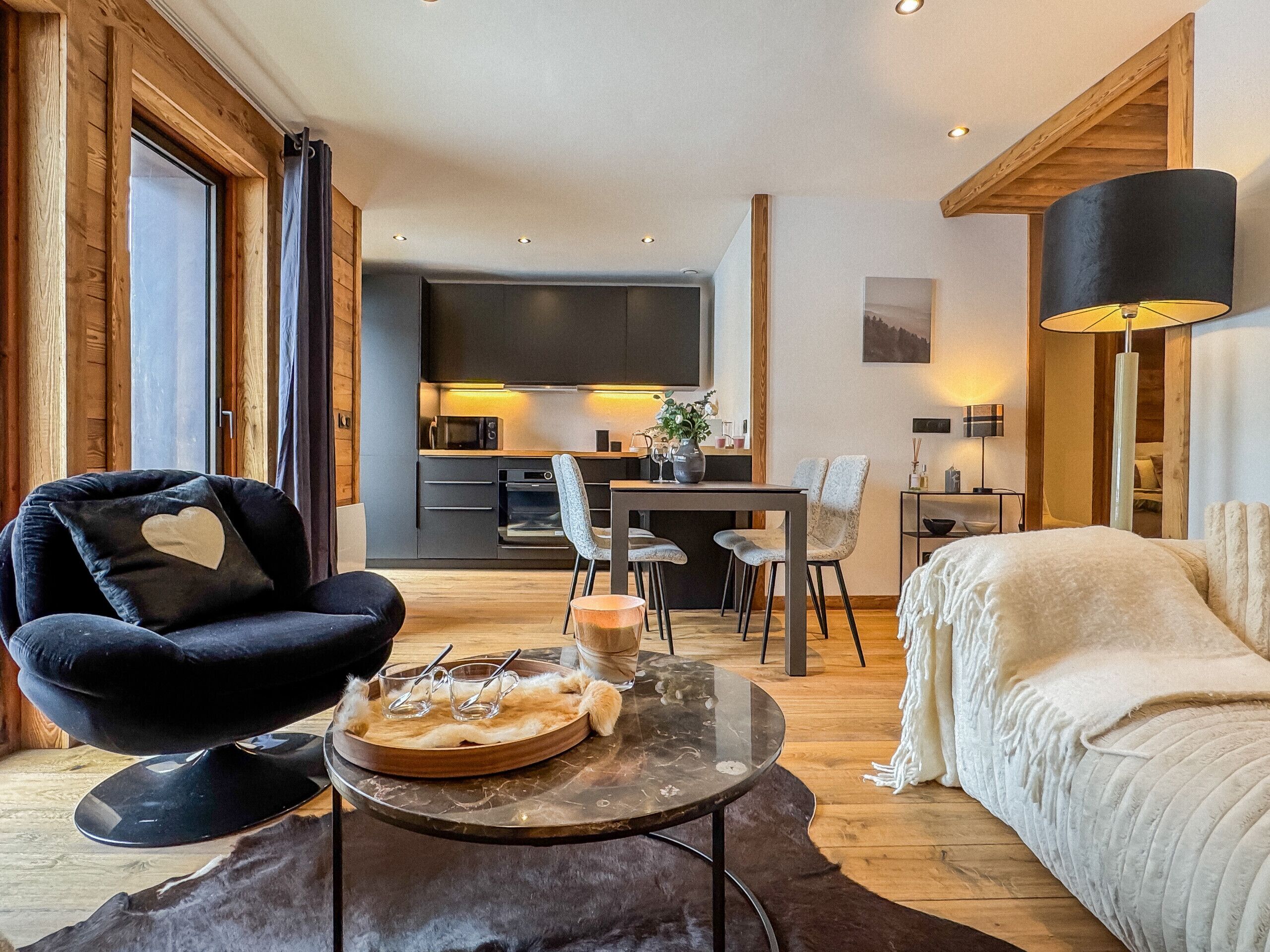 A modern living room with a sofa, a dining area, a kitchen, and a large TV.