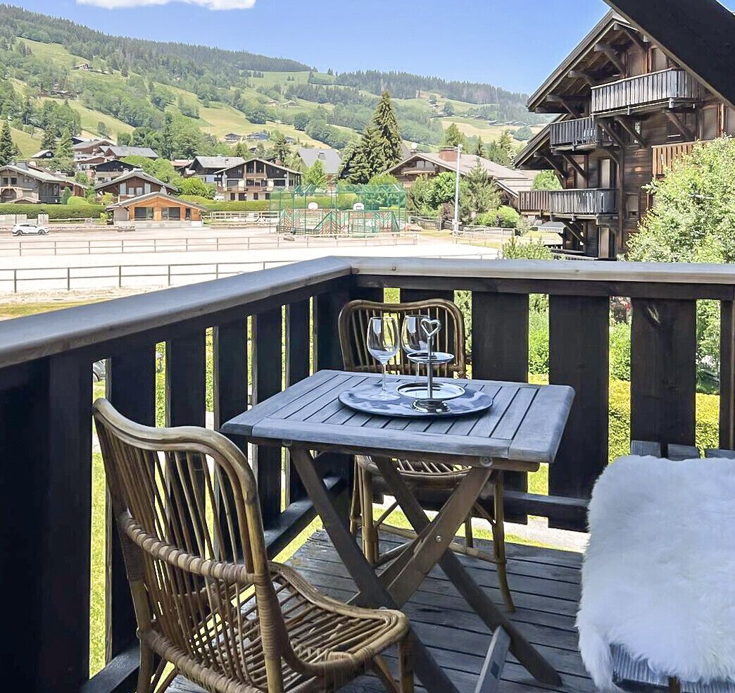 A wooden deck with a table and chairs, overlooking a mountainous landscape.