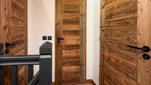 A hallway with wooden doors, a black metal railing, and a white wall. - Lutins Megève Village Sports Arena (Megève)